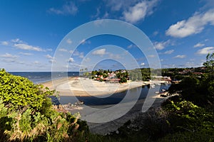 A man going to the edge of a cliff, where one can see the beach and some house.