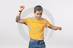 Man going wild, having fun and enjoying life. Attractive asian hipster guy in yellow t-shirt, tattooed, raising hands