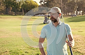 man golfer in cap with golf club on summer green grass, sport