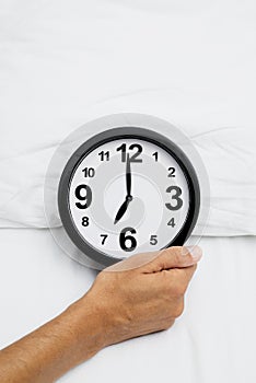 Man grabbing a clock at seven in bed