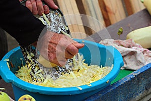 Man grates a squash. Hands hold grater and vegetable