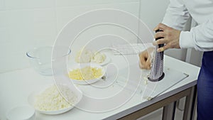 A man is grating cheese; there are other ingredients on the table.
