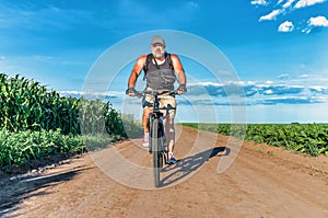 Man with a gray beard rides bicycle on field road. Summer Bike Trip