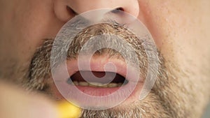 A man with a gray beard swallows a pill from the virus, coronavirus and makes a wry face. Super macro close-up.