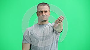 A man in a gray T-shirt, on a green background, close-up, shows his thumbs down