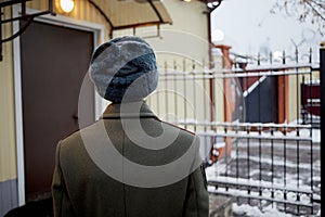 Man in greatcoat stands near checkpoint office and photo