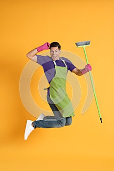 Man with green broom jumping on orange background
