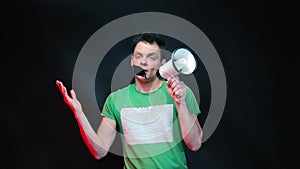 A man in green clothes and a megaphone in his hands shouts.