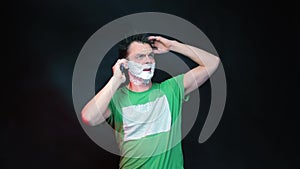 A man in green clothes with shaving foam on his face.