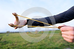 Man in a green field shoots a child`s wooden slingshot, pulls on rubber, toy weapon concept for boys, return to childhood,