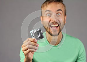 Man in green shirt holds a new condom in hand, joy of found a co