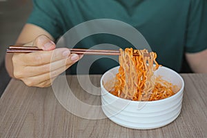 A man in a green t-shirt hold chopsticks with korean style instant noodles. K-pop became a global phenomenon exporting pop culture