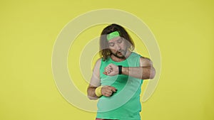 Man in green top and headband running, checking his time results on the smart watch app. Isolated on yellow background.