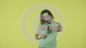 Man in green top and headband running, checking his time results on the smart watch app. Isolated on yellow background