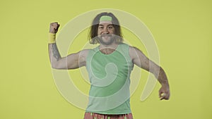 Man in green top and headband showing his muscles, pointingat hand, smiling with thumbs up gesture. Isolated on yellow