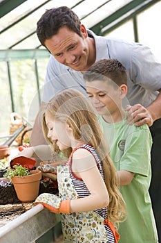 Man in greenhouse helping two young children