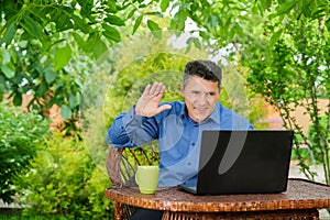 Man greets with hand to business partner via laptop in home garden