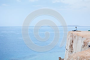 Man greets sunrise of sun on high mountain above sea. Aerial view to calm blue sea with rocky coastline. Panoramic view