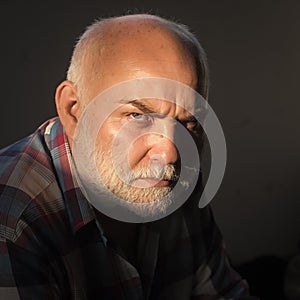 Man with grey beard, frown brows on serious face