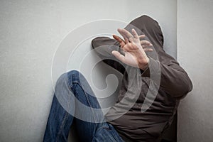 Man in grey hood sitting in the corner and hiding his face with the hands, show stop sign