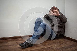 Man in grey hood sitting in the corner and hiding his face with the hands, show stop sign