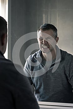 Man in grey polar fleece staring at himself in bathroom mirror