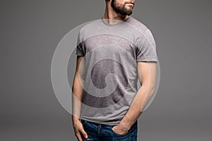 A man in a grey t-shirt and denims holds his hands in pockets.