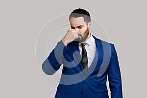 Man grimacing with disgust, holding breath, pinching nose with fingers to avoid bad smell awful odor