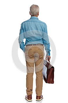 Man with grizzle hair holding in one hand suitcase and the other one in pocket