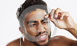 Man grooming his eyebrows with a tweezer in studio for self care, beauty and cleanliness. Hair removal, tweezing and