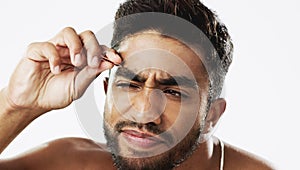 Man grooming his eyebrows with a tweezer in studio for self care, beauty and cleanliness. Hair removal, tweezing and