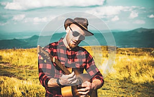 Man with guitar on nature. Hipster plays guitar on Camping holiday.