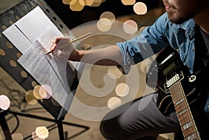 Man with guitar writing to music book at studio