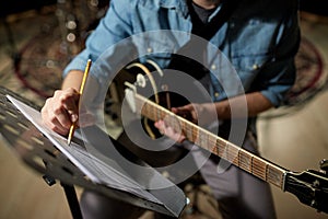 Man with guitar writing to music book at studio