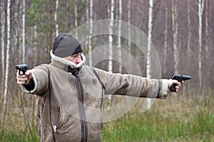 A man with a gun outdoor. The criminal shoots a pistol. Bandit on the road