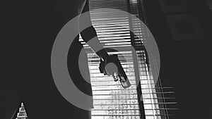 A man with a gun is standing by the window blind ,ready to protect himself from another bad people, b&w crime scene conceptual.