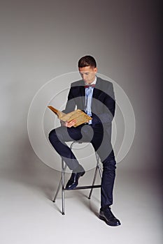 a man, a guy in a blue suit, sits on a chair and reads an old book, the concept of knowledge, study, science, business, everything