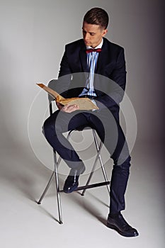 A man, a guy in a blue suit, sits on a chair and reads an old book, the concept of knowledge, study, science, business, everything