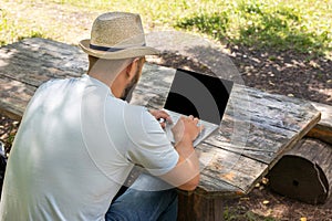 Man or guy working on a computer with a blank screen for copy space, sitting on a bench in the summer outdoors