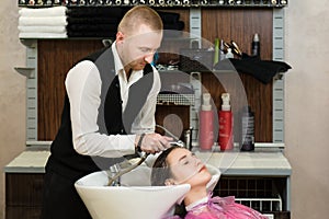 Man hair master watering a girl`s hair with a shower in a hair studio