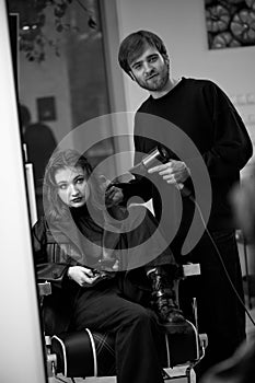 man hairdresser dries female hair with hairdryer after washing