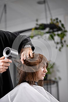 man hairdresser dries female hair with hairdryer after washing