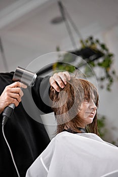 man hairdresser dries female hair with hairdryer after washing