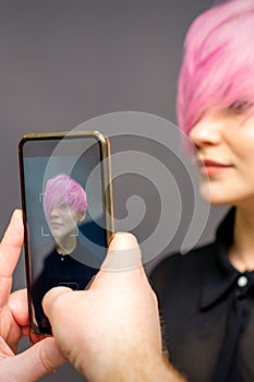 Man hairdresser& x27;s hands taking picture on smartphone of her client short pink hairstyle.