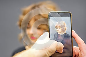 Man hairdresser taking pictures on the smartphone of her client& x27;s hairstyle against a gray background.