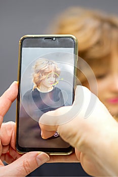 Man hairdresser taking pictures on the smartphone of her client& x27;s hairstyle against a gray background.