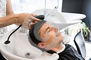 Man hairdresser washing head of a handsome smiling client
