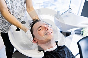 Man hairdresser wiping head of a handsome smiling client with a towel at the barbershop.