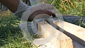 Man hammering used long nail into old boards