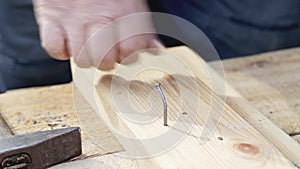 A man hammers a bent nail into wooden planks, close-up. Profession